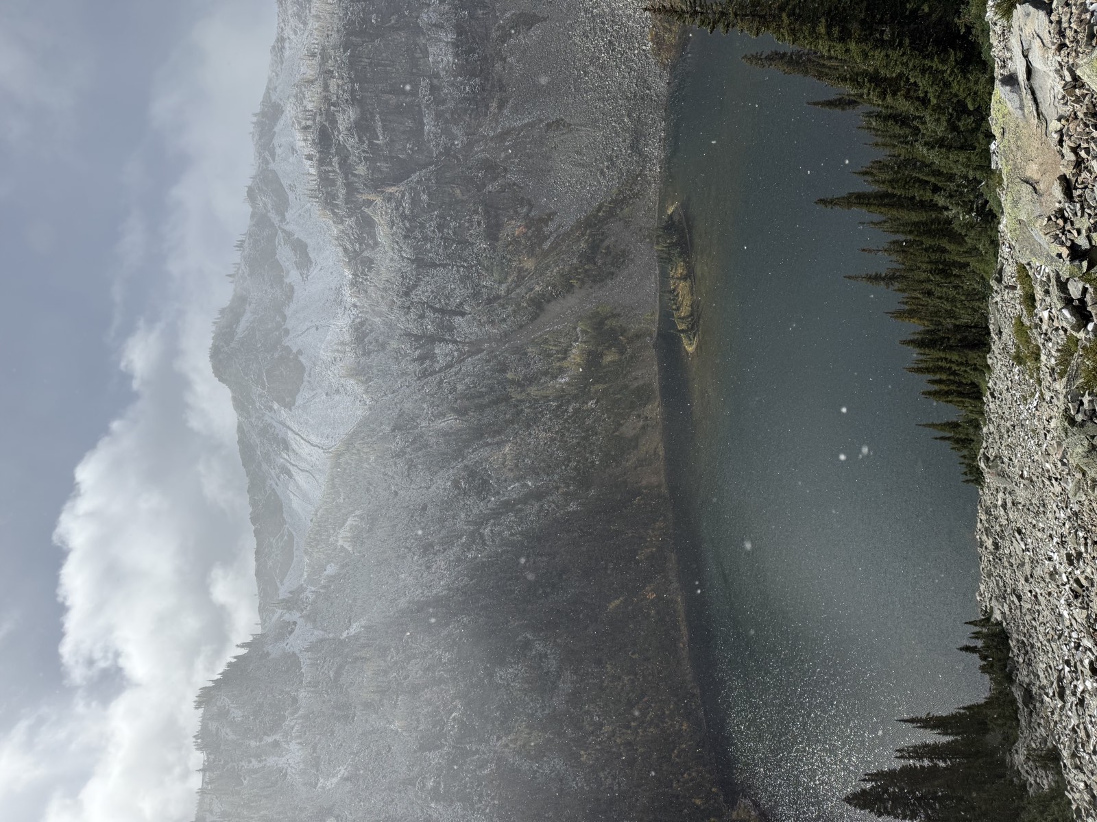 Lake Ann and its small island below snow-dusted cliffs, with snowflakes in the air