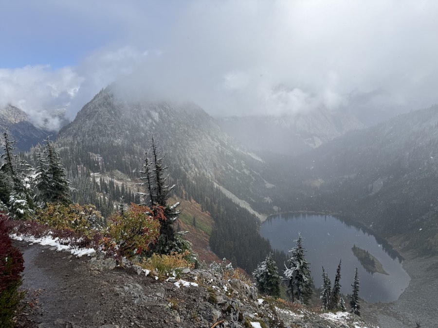 Lake Ann far below a snow-dusted trail on the Maple Pass Loop