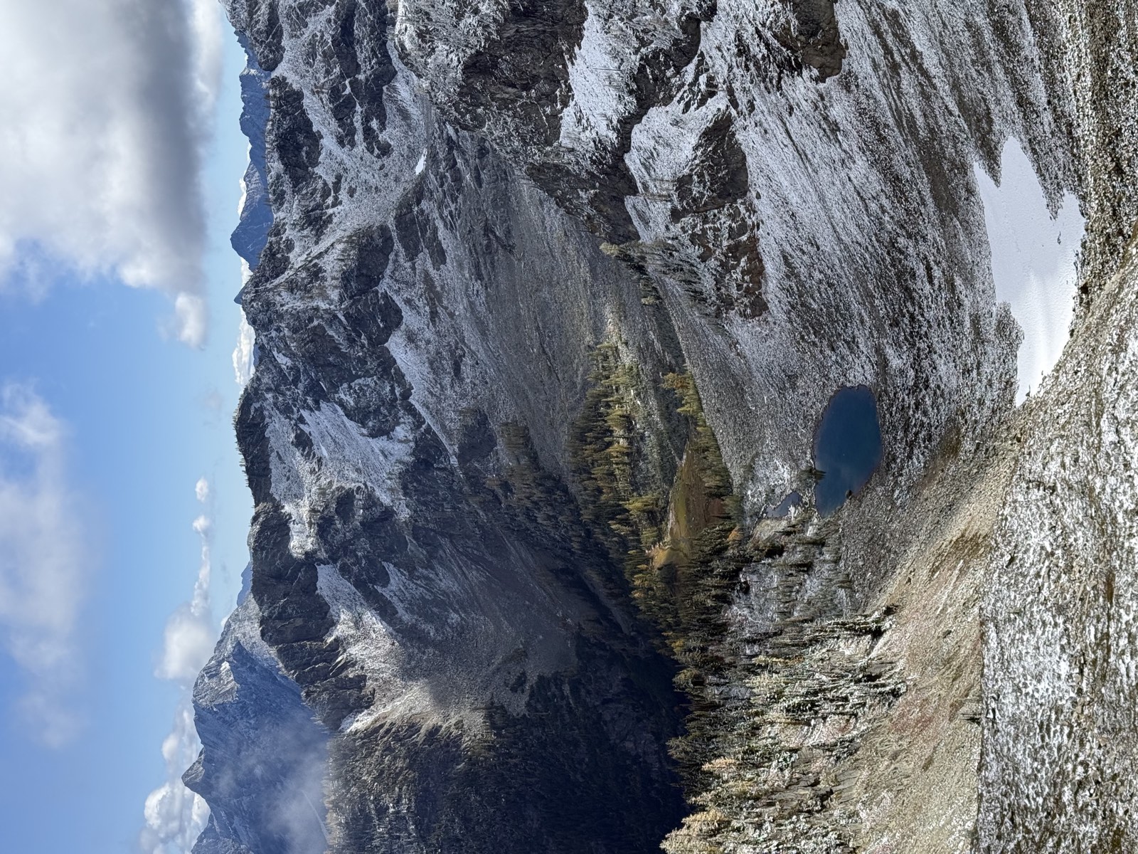 Blue sky over snowy peaks and a small blue tarn in a rocky basin