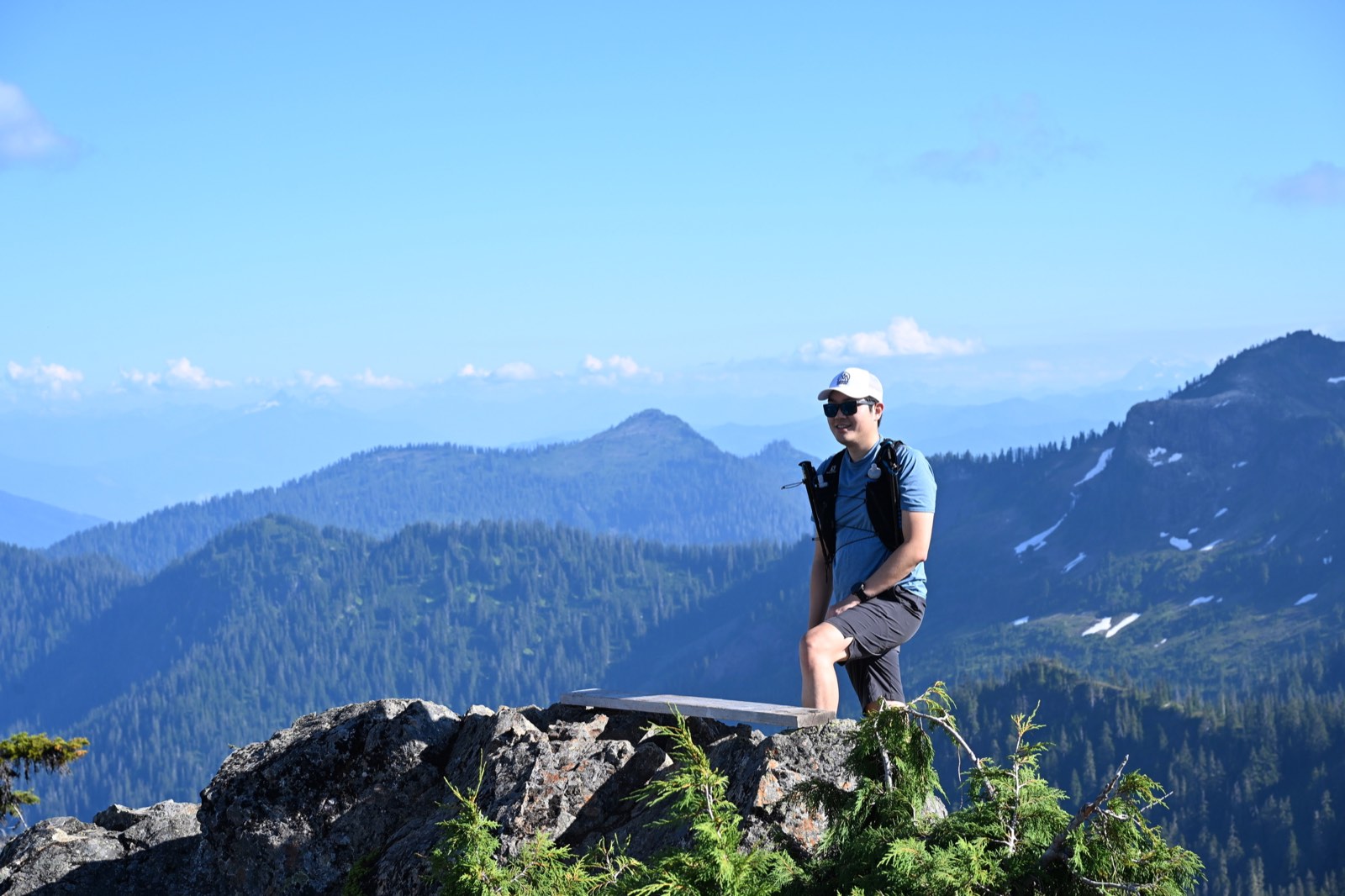 A hiker resting on a rocky outcrop with forested ridges fading into the distance