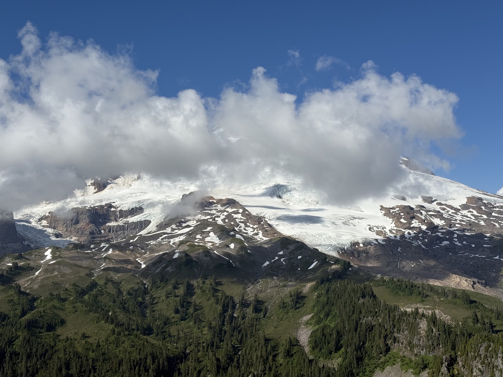 Cloud streaming across the glaciated upper slopes of Mount Baker above forested ridges