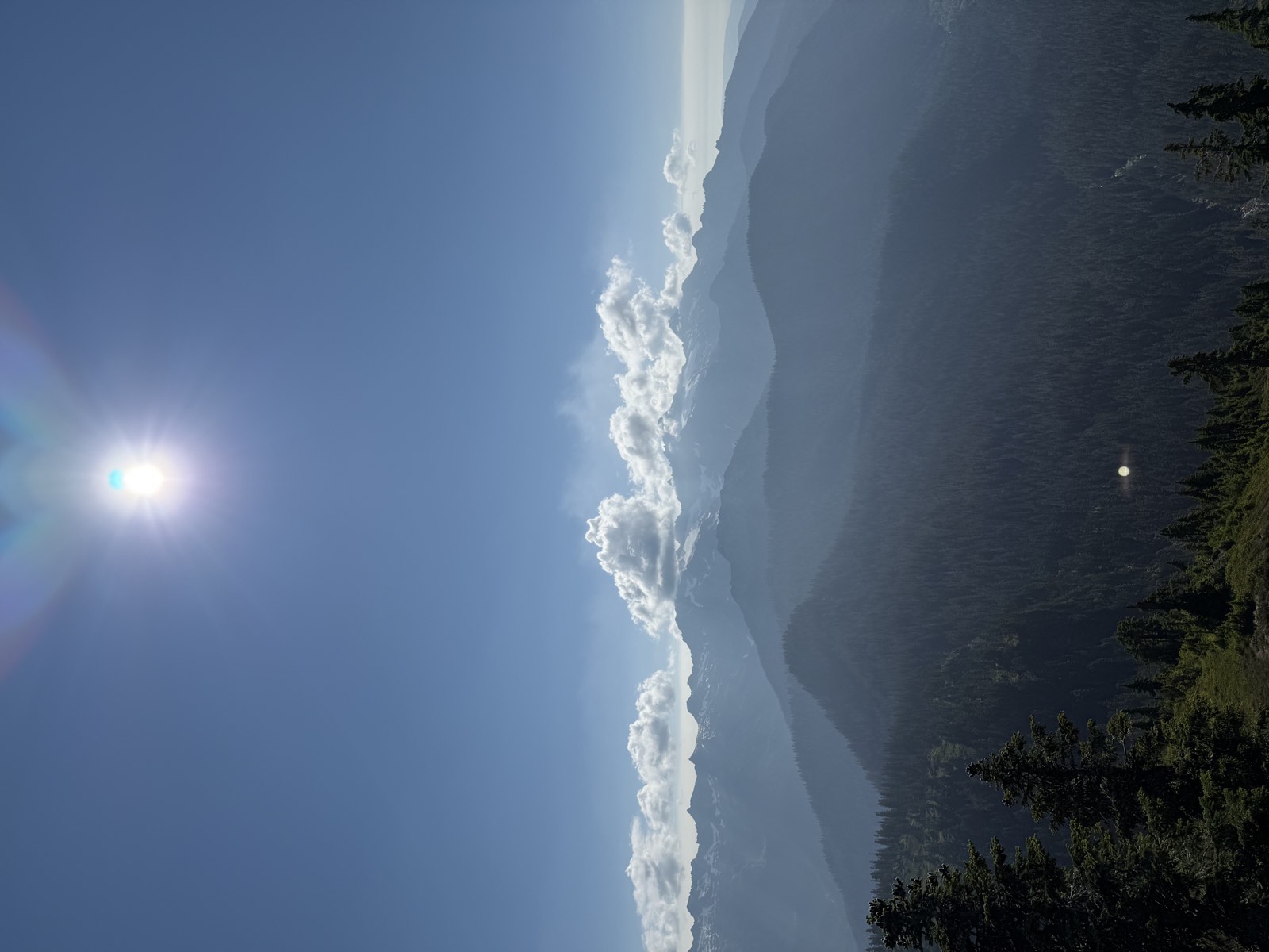 Hazy layers of forested ridges with distant snowy peaks under a bright sun