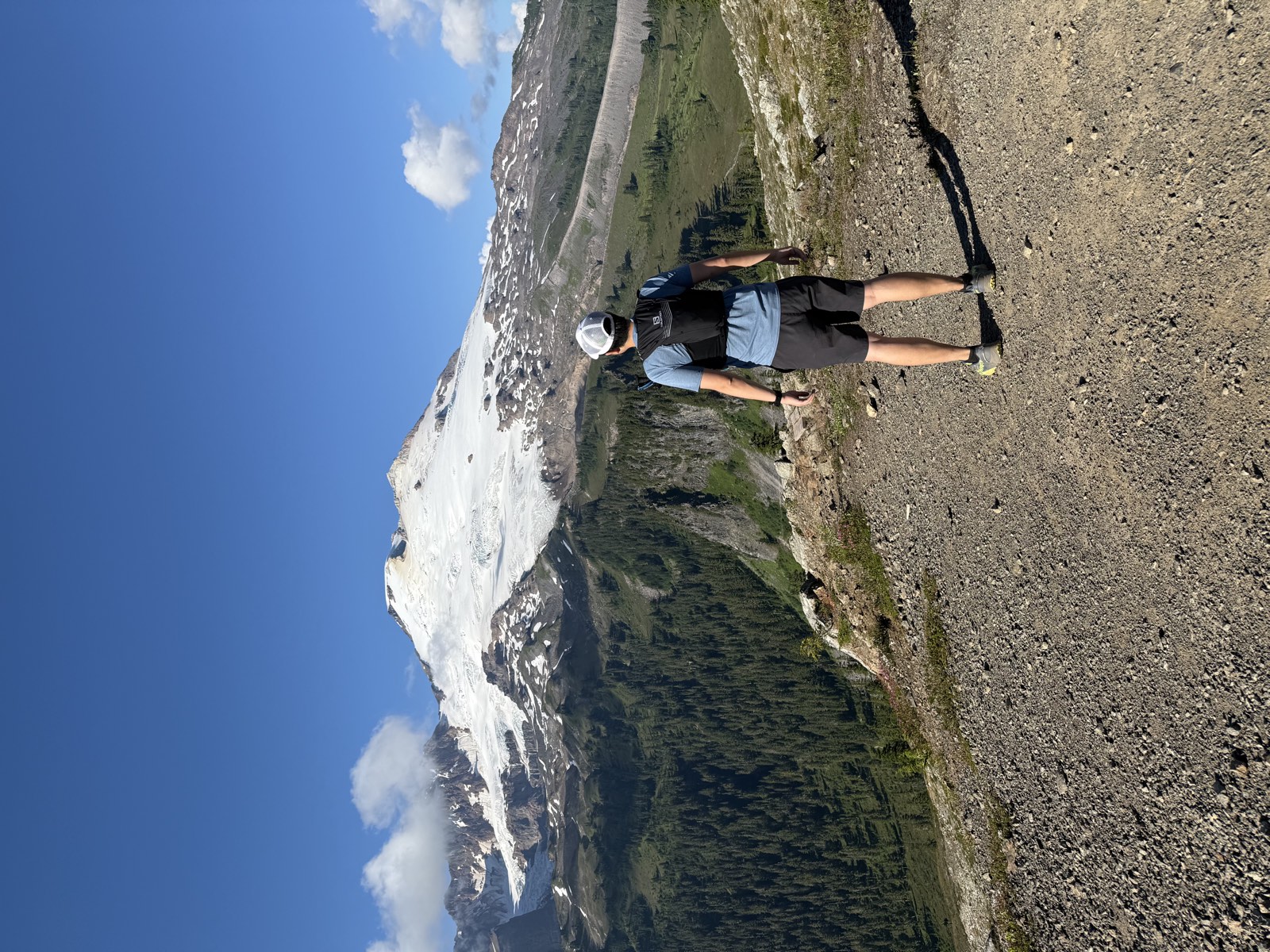 A hiker walking a wide gravel trail toward snow-covered Mount Baker