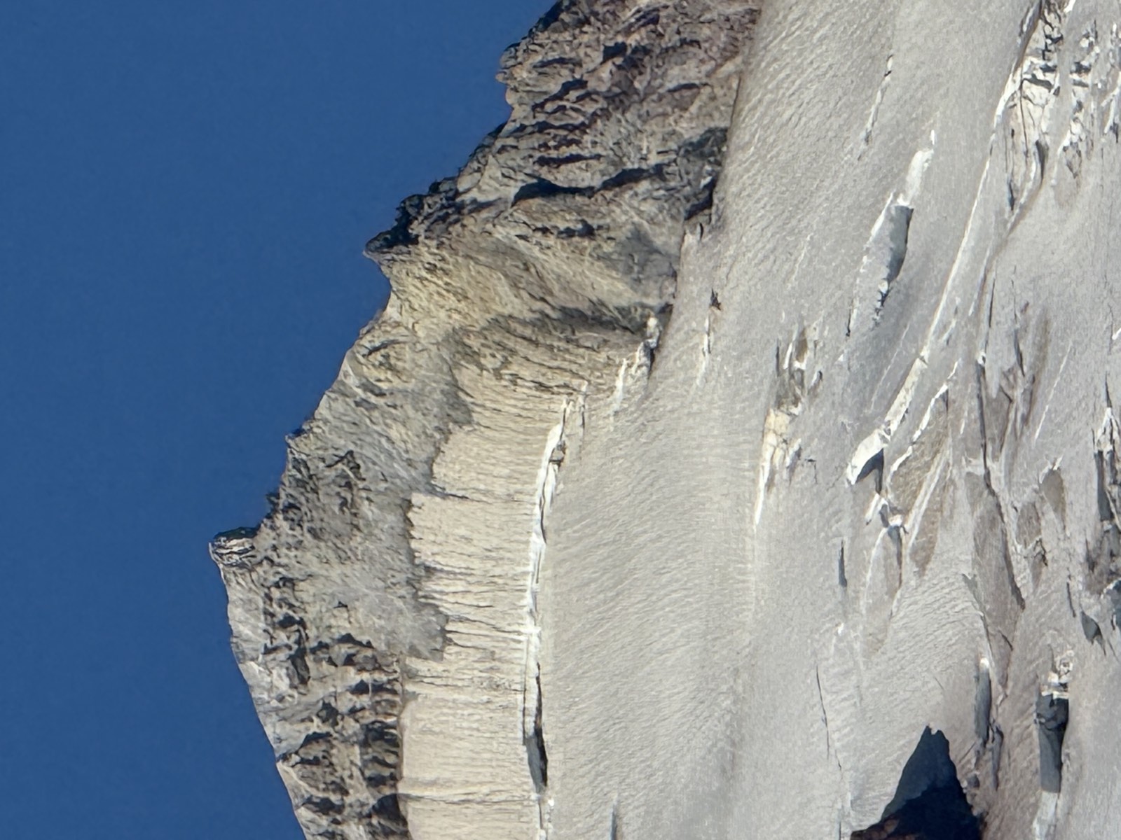 A close view of a rocky summit crest rising above a broad snowfield