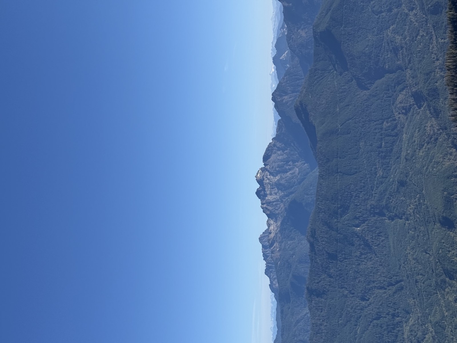 A craggy gray peak rising above a long forested ridge