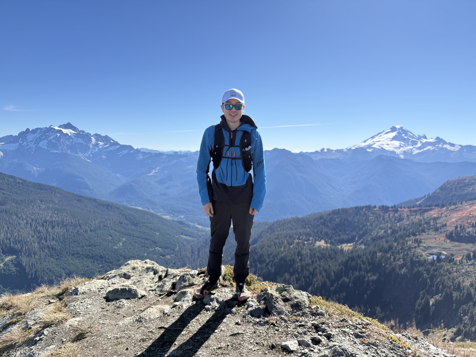 Bruce standing on top of Yellow Aster Butte, with Mount Shuksan and Mount Baker behind